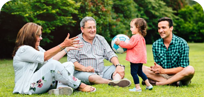 Family sitting down at a park playing with their kid holding a ball