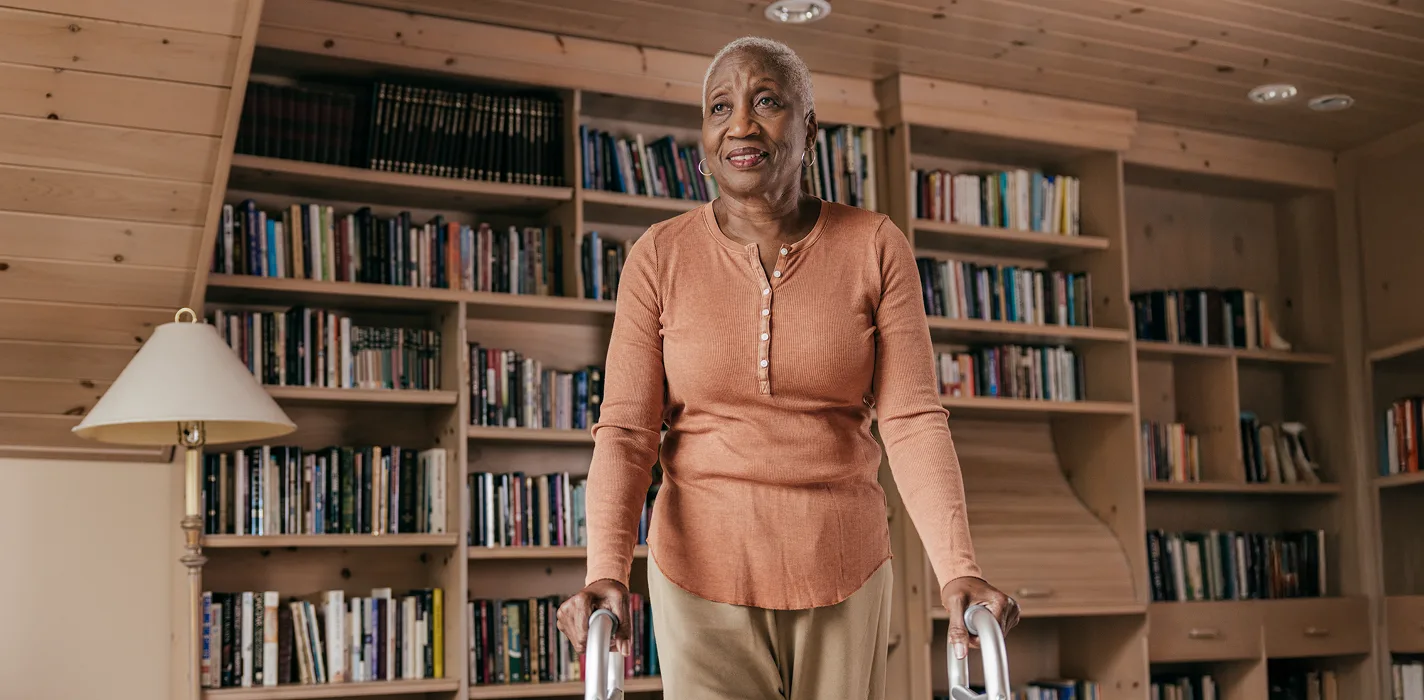 older black African American female smilingin front of a bookshelf, she's using a walker